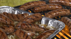 Bratwurst in a foil pan and bratwursts on a flame grill