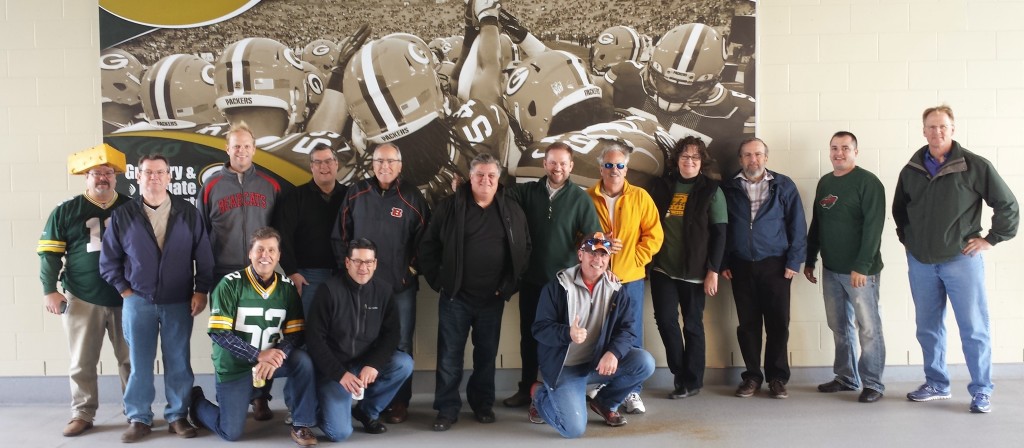 Dorner Channel Members pose group photo in front of packers team photo at stadium