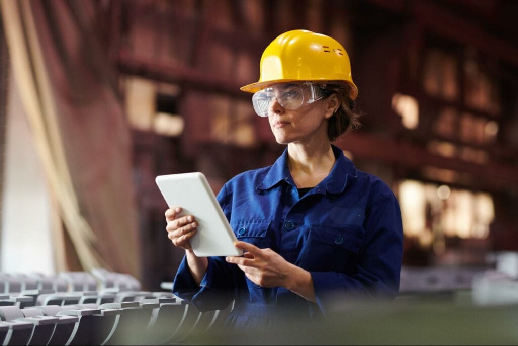 A woman in a blue utility suit and a yellow hard hat assesses the safety of her operation.