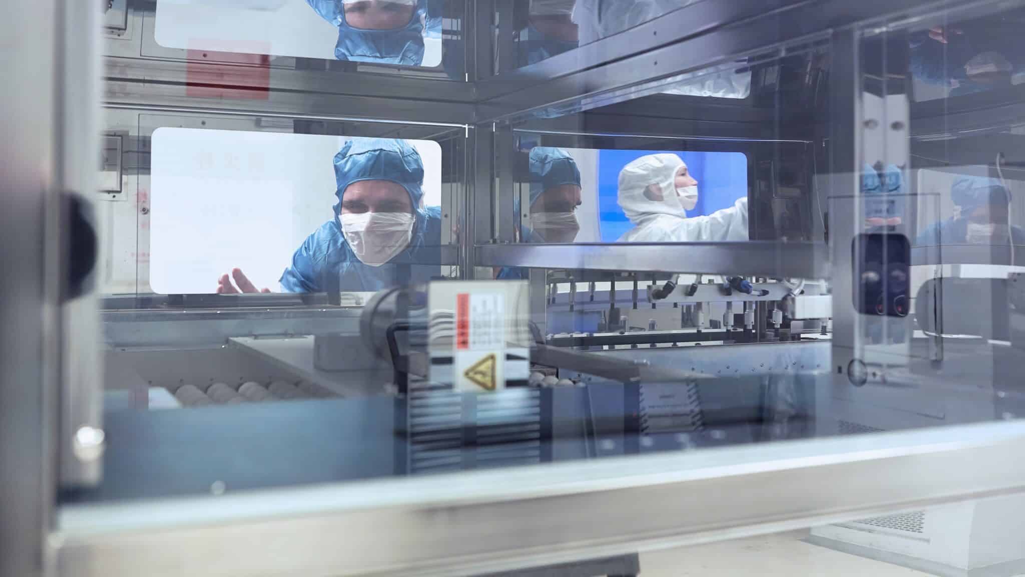 Male worker looking through manufacturing machine window in flexible electronics factory clean room