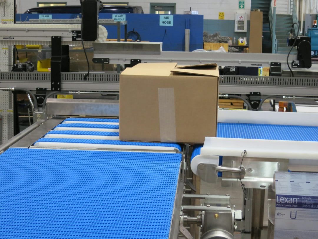 A cardboard box is transported along a blue-belted conveyor as part of a material handling system.