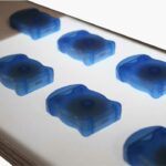 Orderly translucent blue objects passing over a backlit section of conveyor.