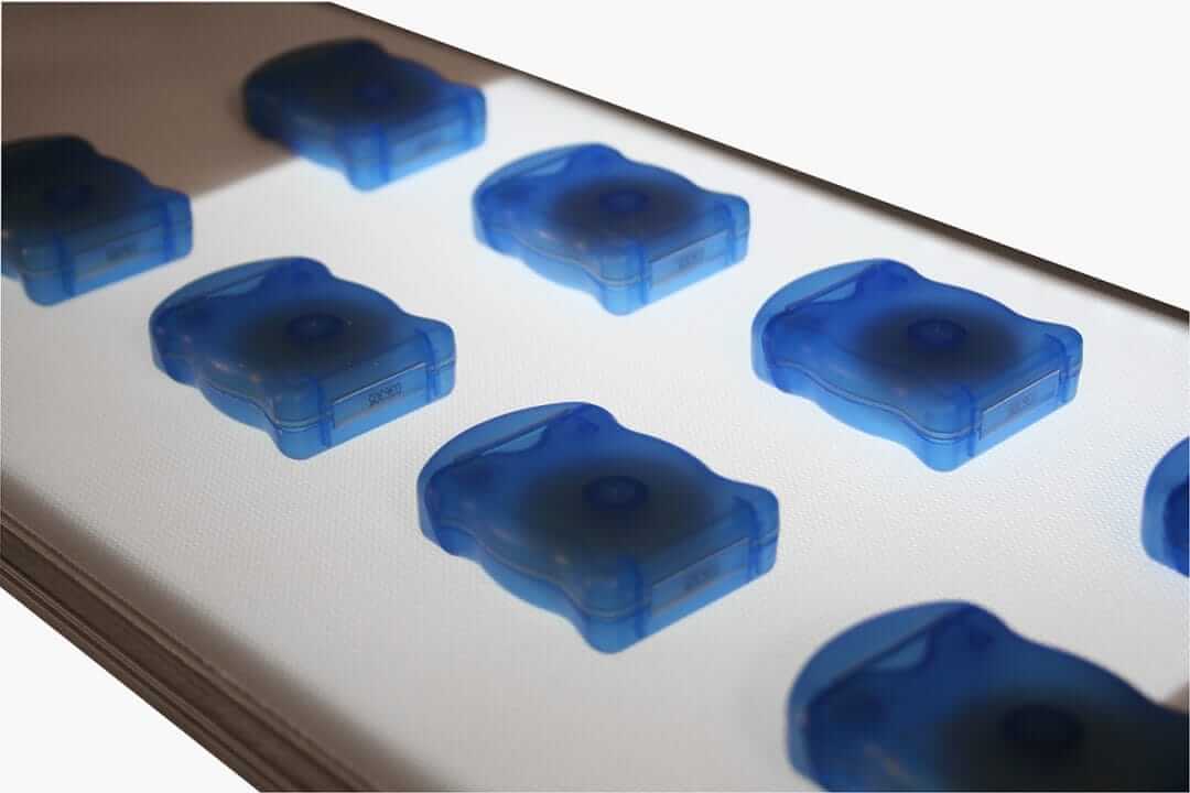 Orderly translucent blue objects passing over a backlit section of conveyor.